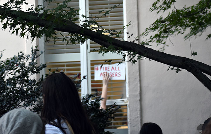 Protestor holds a sign that reads "# fire all abusers" to a window on the Osborne Administrative Building at UofSC