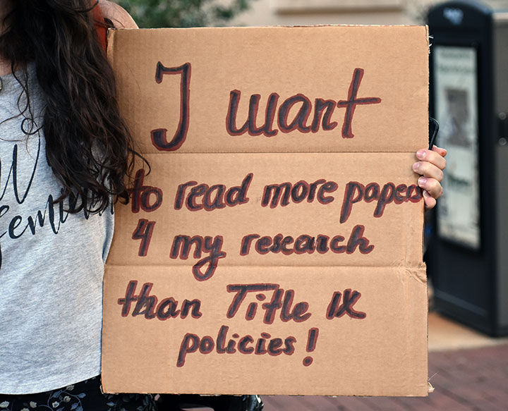 Protestor holds a sign that reads "I want to read more papers 4 my research that Title IX policies!"