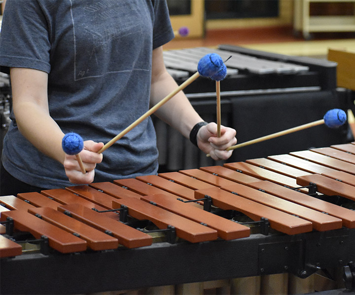 An up close image of a marimba that a young woman is playing with four mallets.