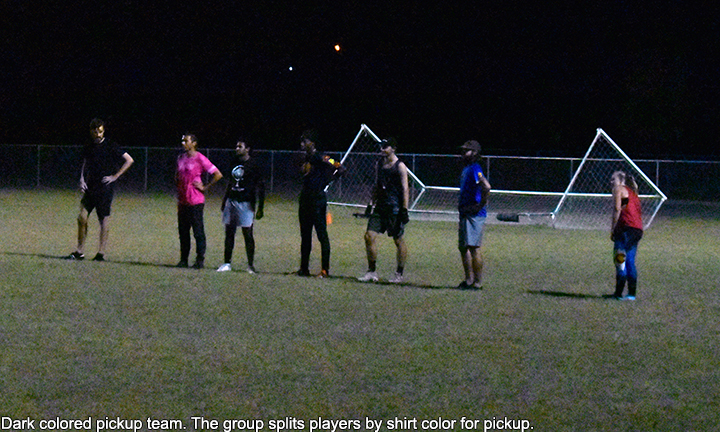 Photo of players with dark colored shirts lined up, ready to start frisbee match