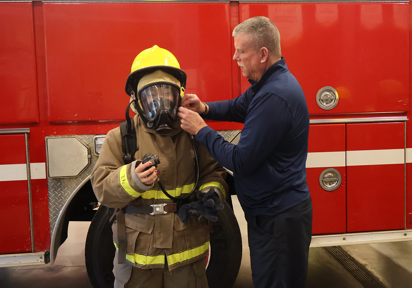 Mike Greer helps a student adjust her firefighter gear.