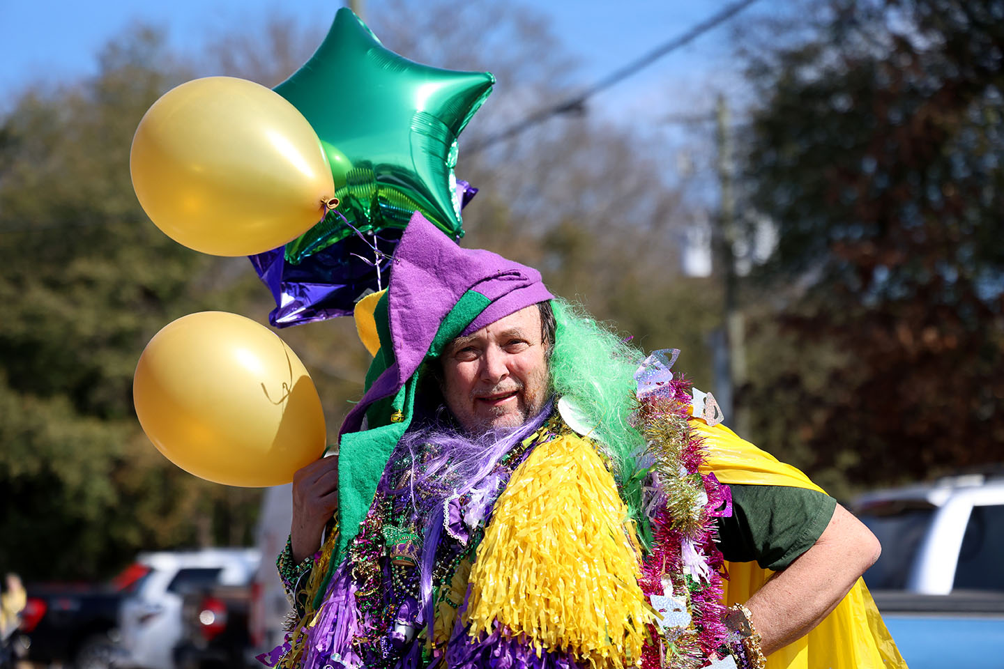Mardi Gras_HC_1035cc_small Dwayne Schumpert is wearing plastic bead necklaces, a traditional Mardi Gras accessory, in the colors green, purple, and yellow. His costume consists mostly of tinsel and a green wig, plus pink tinsel and a mask that resembles the Mardi Gras theme. He has a purple-and-green star balloon and two round yellow balloons attached to him as well.