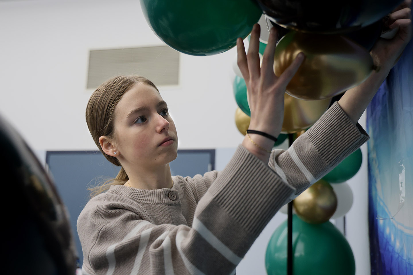 SouperBowl_HC_0691cc_small Claire Campbell holds a gold balloon to add to the balloon arch. The balloon arch has black, gold, and green balloons.