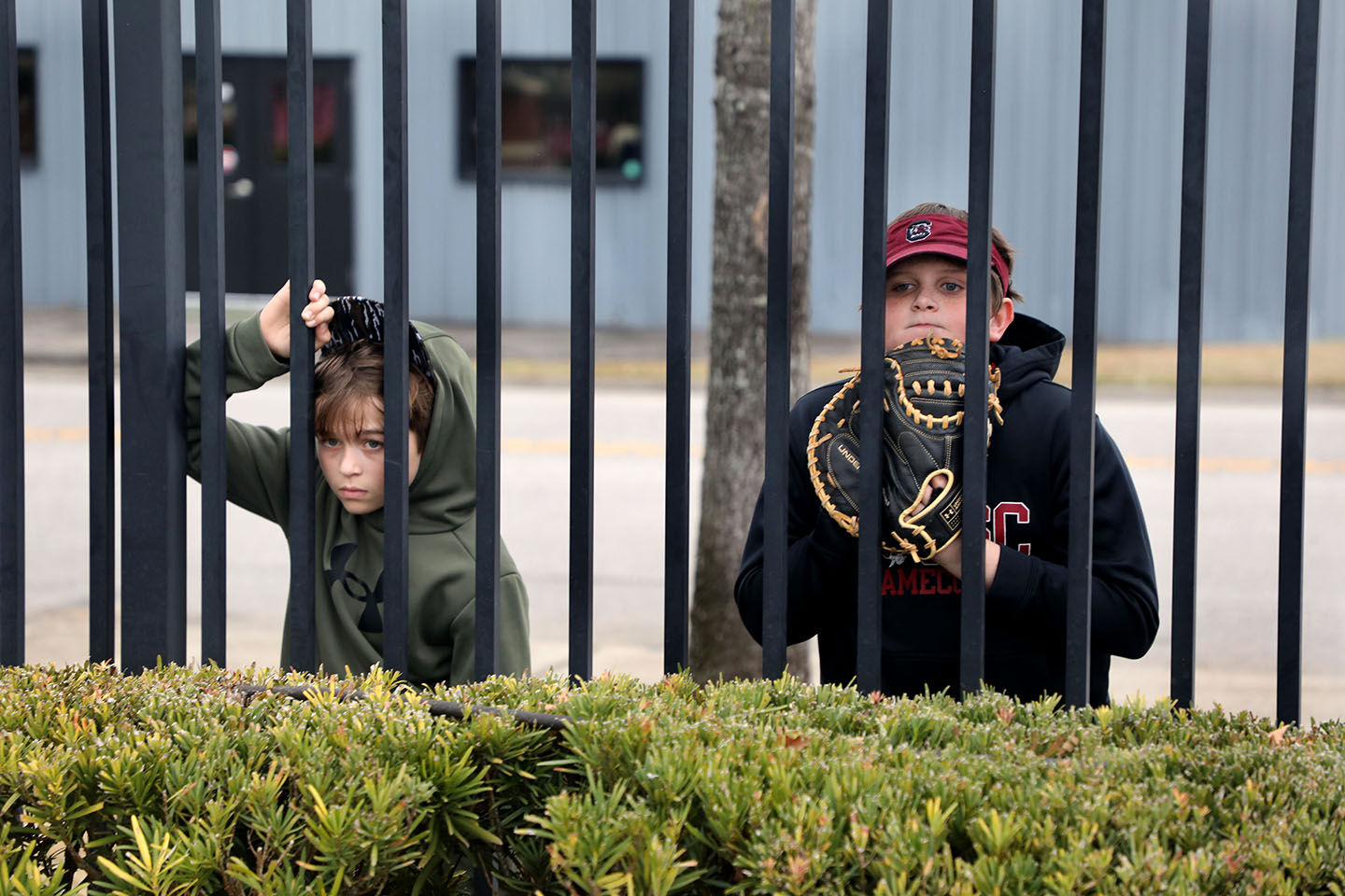 Two boys with baseball mitts wait behind a fence for the gates to open.