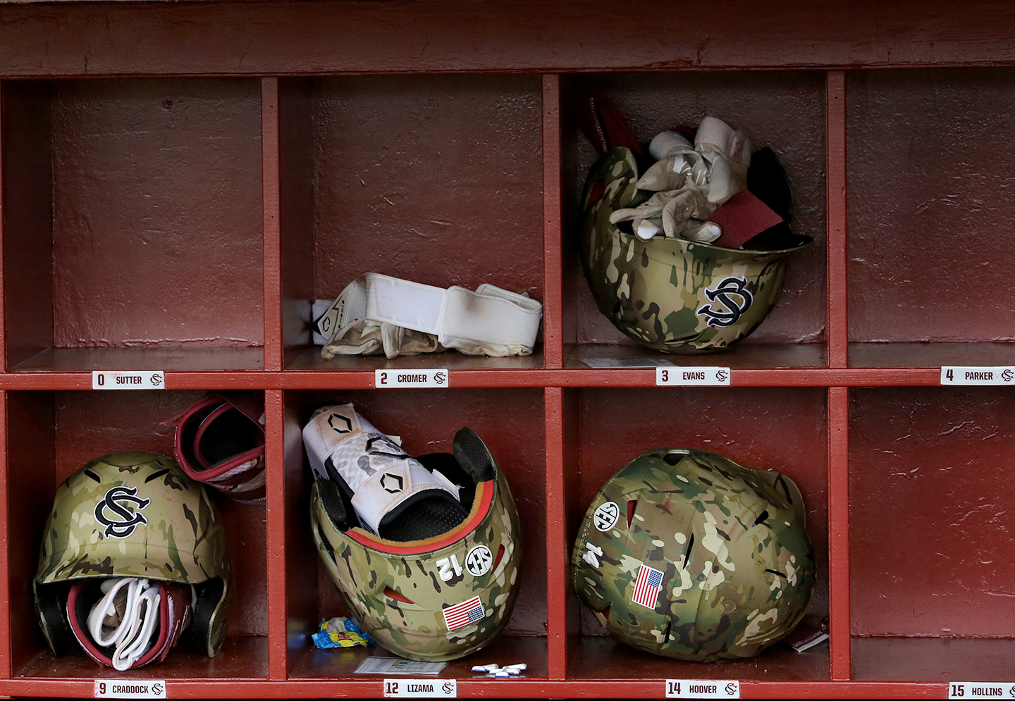 Camouflage baseball helmets sit in cubbies.
