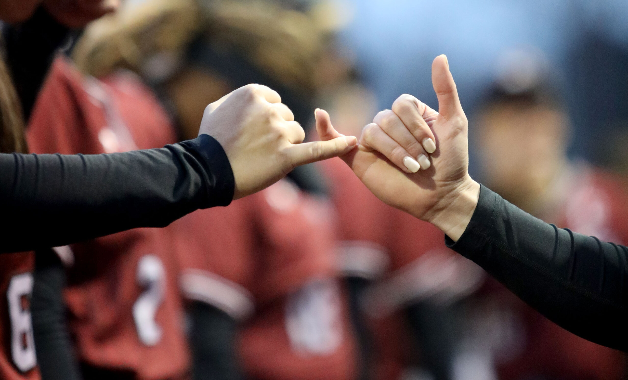 A closeup of two hands shows players grasping the pinkie fingers of the other. 