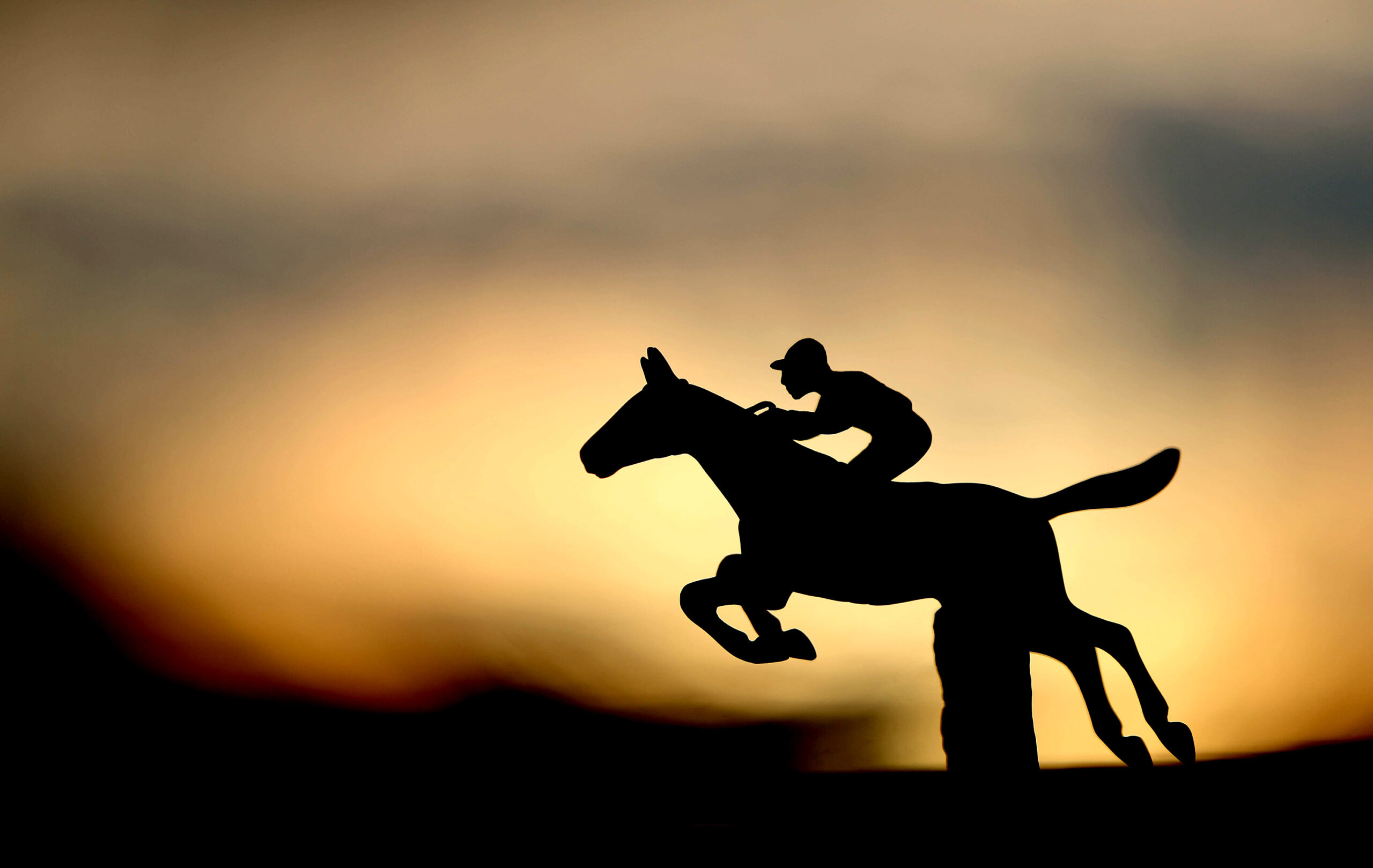 A hood ornament in the shape of a jockey on a horse jumping a hurdle adorns a truck by the stables